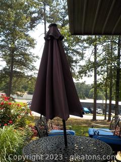 Pretty Purple Patio Table Umbrella, with Base.  Has Lights Under Canopy.  Rolls Closed for Storage. Only leaning due to leaning surface placement  